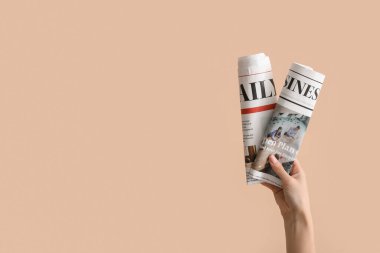 Bej arka planda sarılmış gazeteleri olan kadın.