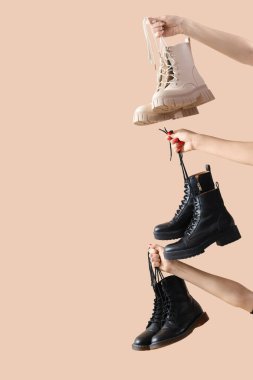 Bej arka planda farklı çizmeler tutan kadın eller.