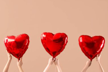 Bej arka planda kalp şeklinde balonlar tutan kadın eller. Sevgililer Günü kutlaması