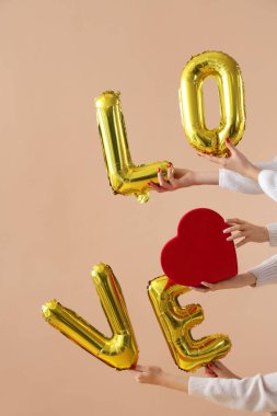 Kalp şeklinde hediye kutusu tutan kadın eller ve bej arka plandaki balonlardan yapılmış aşk kelimesi. Sevgililer Günü kutlaması