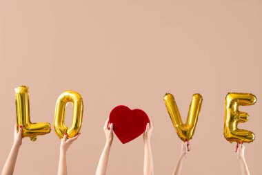 Kalp şeklinde hediye kutusu tutan kadın eller ve bej arka plandaki balonlardan yapılmış aşk kelimesi. Sevgililer Günü kutlaması