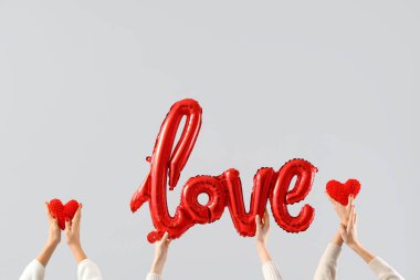 Kalpleri tutan kadın eller ve beyaz arka plandaki balonlardan yapılmış kelime aşkı. Sevgililer Günü kutlaması