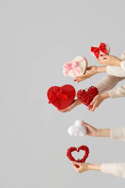 Kadın elleri farklı kalp şeklinde hediye kutuları ve beyaz arka planda kalpler tutuyor. Sevgililer Günü kutlaması