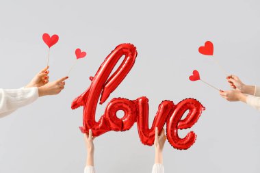 Kağıt kalp tutan kadın eller ve beyaz arka plandaki balonlardan yapılmış aşk sözcükleri. Sevgililer Günü kutlaması