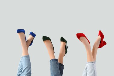 Gri arka planda farklı ayakkabılar giyen kadın bacakları.