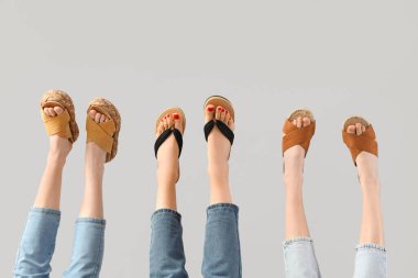 Gri arka planda farklı sandaletler giyen kadın bacakları.