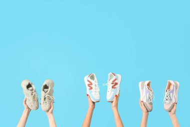 Mavi arka planda farklı spor ayakkabıları tutan kadın eller.
