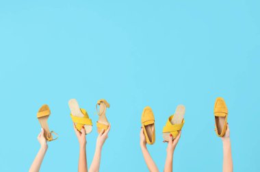 Mavi arka planda farklı sandaletler tutan kadın eller.