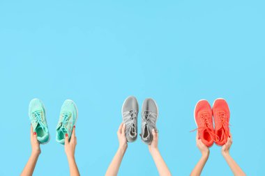 Mavi arka planda farklı spor ayakkabıları tutan kadın eller.