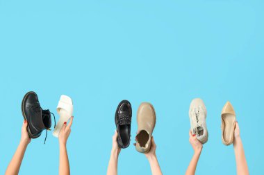 Mavi arka planda farklı ayakkabılar tutan kadın eller.