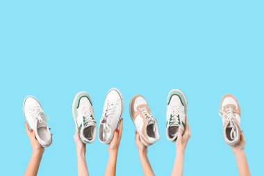 Mavi arka planda farklı spor ayakkabıları tutan kadın eller.