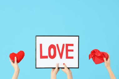 Çerçeveyi aşk sözcüğü, hediye kutusu ve kalbi mavi arka planda tutan kadın elleri. Sevgililer Günü kutlaması