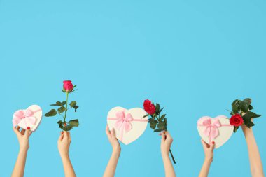 Kalp şeklinde hediye kutuları ve mavi arka planda güller tutan kadın elleri. Sevgililer Günü kutlaması