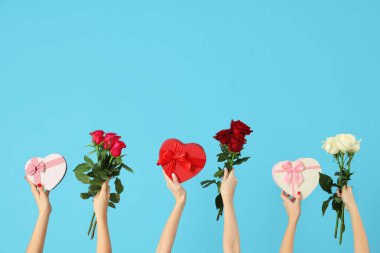 Kalp şeklinde hediye kutuları ve mavi arka planda güller tutan kadın elleri. Sevgililer Günü kutlaması