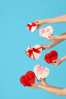 Mavi arka planda kalp şeklinde farklı hediye kutuları tutan kadın elleri. Sevgililer Günü kutlaması