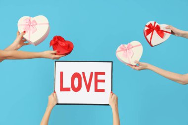 Mavi arka planda aşk ve kalp şeklinde hediye kutularıyla çerçeveyi tutan kadın eller. Sevgililer Günü kutlaması