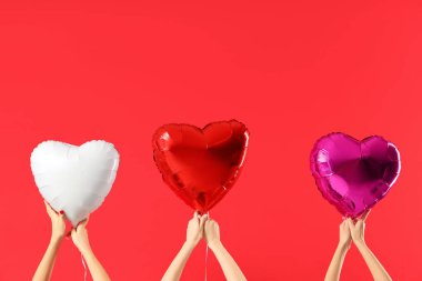 Kırmızı arka planda kalp şeklinde balonlar tutan kadın eller. Sevgililer Günü kutlaması