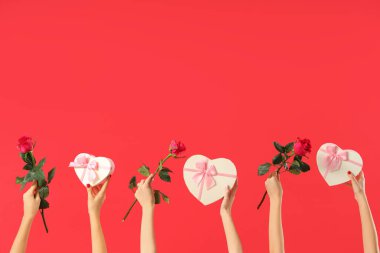 Kalp şeklinde hediye kutuları ve kırmızı arka planda güller tutan kadın elleri. Sevgililer Günü kutlaması