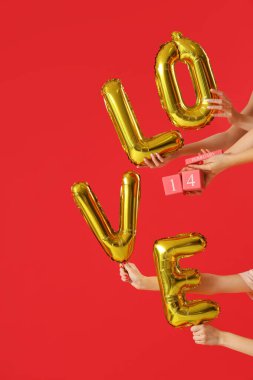 Küp takvimi tutan kadın eller ve kırmızı arka plandaki balonlardan yapılmış kelime aşkı. Sevgililer Günü kutlaması