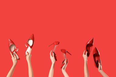Kırmızı arka planda farklı ayakkabılar tutan kadın eller.