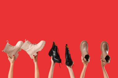 Kırmızı arka planda farklı çizmeler tutan kadın eller.