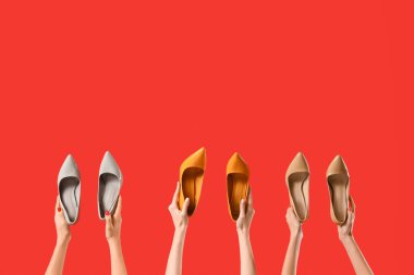 Kırmızı arka planda farklı ayakkabılar tutan kadın eller.