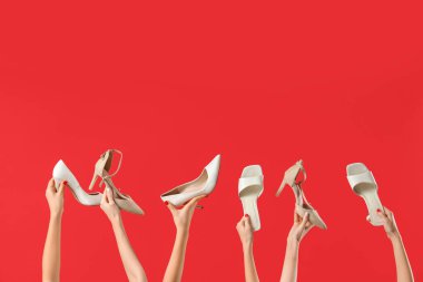 Kırmızı arka planda farklı ayakkabılar tutan kadın eller.