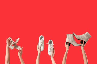 Kırmızı arka planda farklı ayakkabılar tutan kadın eller.