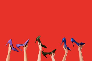 Kırmızı arka planda farklı ayakkabılar tutan kadın eller.