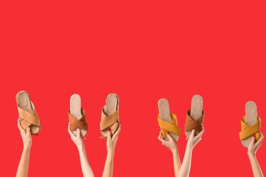 Kırmızı arka planda farklı sandaletler tutan kadın eller.