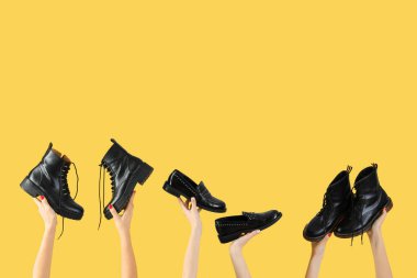 Sarı arka planda farklı ayakkabılar tutan kadın eller.