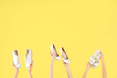 Sarı arka planda farklı ayakkabılar tutan kadın eller.