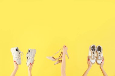 Sarı arka planda farklı ayakkabılar tutan kadın eller.