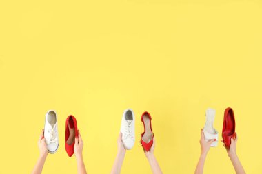 Sarı arka planda farklı ayakkabılar tutan kadın eller.