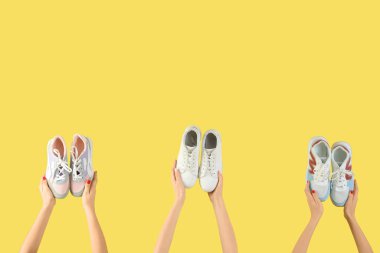 Sarı arka planda farklı spor ayakkabıları tutan kadın eller.