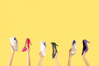Sarı arka planda farklı ayakkabılar tutan kadın eller.