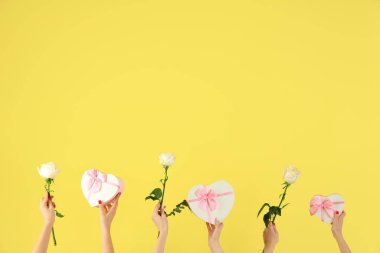 Kalp şeklinde hediye kutuları ve sarı arka planda güller tutan kadın elleri. Sevgililer Günü kutlaması