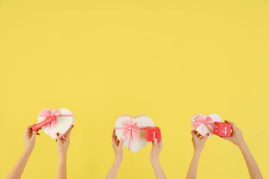 Kalp şeklinde hediye kutuları ve 14 Şubat tarihli sarı arkaplanlı küp takvim tutan kadın elleri. Sevgililer Günü kutlaması