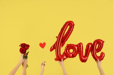 Balonlardan, kağıttan kalplerden ve sarı arka planda güllerden yapılmış aşkı kucaklayan kadın elleri. Sevgililer Günü kutlaması