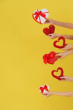 Kalp şeklinde hediye kutuları ve sarı arka planda kalpler tutan kadın elleri. Sevgililer Günü kutlaması