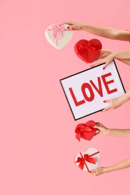 Kadın elleri çerçeveyi pembe arka planda aşk ve kalp şeklinde hediye kutularıyla tutuyor. Sevgililer Günü kutlaması
