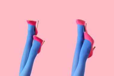 Mavi taytlı kadın bacakları pembe arka planda şık topuklu ayakkabılar giyiyor.