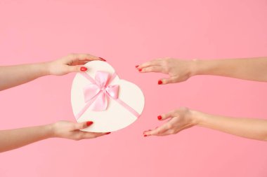 Pembe arka planda kalp şeklinde hediye kutusu olan kadın elleri. Sevgililer Günü kutlaması