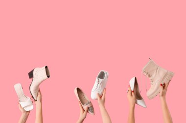 Pembe arka planda farklı ayakkabılar tutan kadın eller.