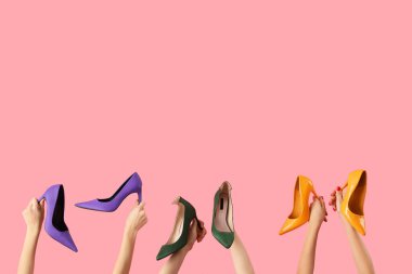 Pembe arka planda farklı şık ayakkabılar tutan kadın eller.