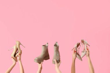 Pembe arka planda farklı ayakkabılar tutan kadın eller.