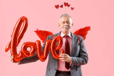 Aşk tanrısı gibi giyinmiş olgun bir adam pembe arka planda balonlardan yapılmış bir aşk sözcüğü. Sevgililer Günü kutlaması
