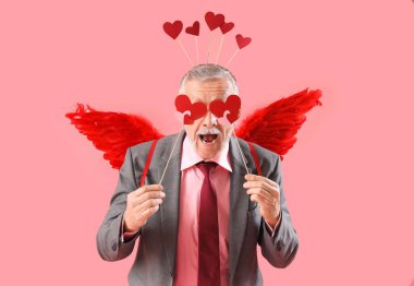 Aşk tanrısı gibi giyinmiş, pembe arka planda kalpleri olan olgun bir adam. Sevgililer Günü kutlaması