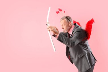 Aşk tanrısı gibi giyinmiş olgun bir adam pembe arka planda ok atıyor. Sevgililer Günü kutlaması