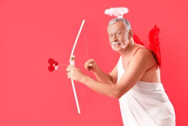 Aşk tanrısı gibi giyinmiş olgun bir adam kırmızı arka planda ok atıyor. Sevgililer Günü kutlaması